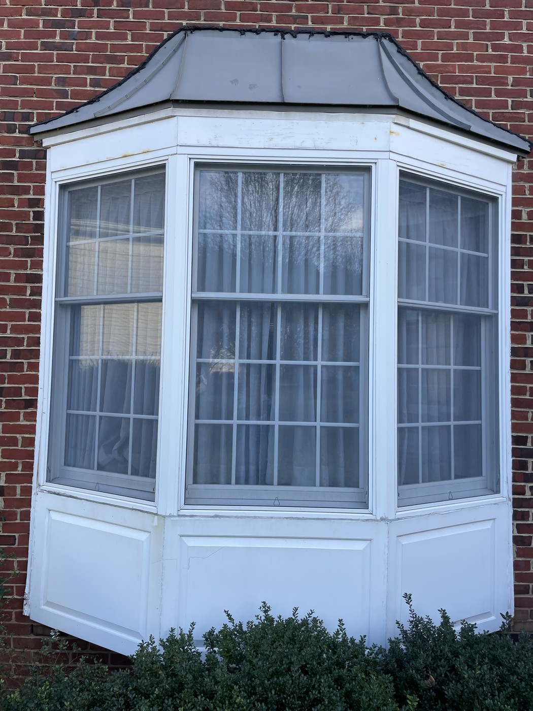 Brick exterior bay window with sheer curtains, before